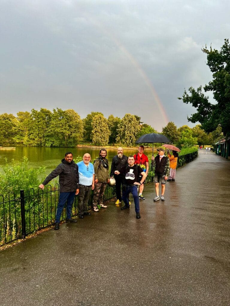 Men on walk smiling for camera in park, with rainbow in sky