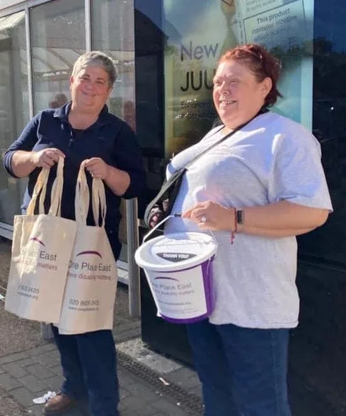 Two smiling people raising money for One Place East by collecting donations and selling custom bags.