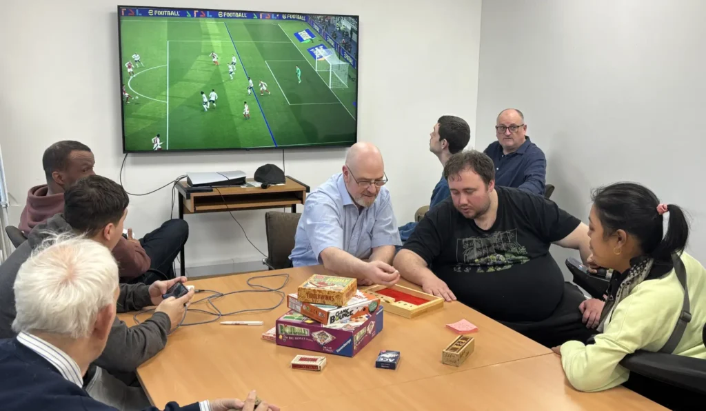 People playing board games and a football game on a ps5 and big screen TV.