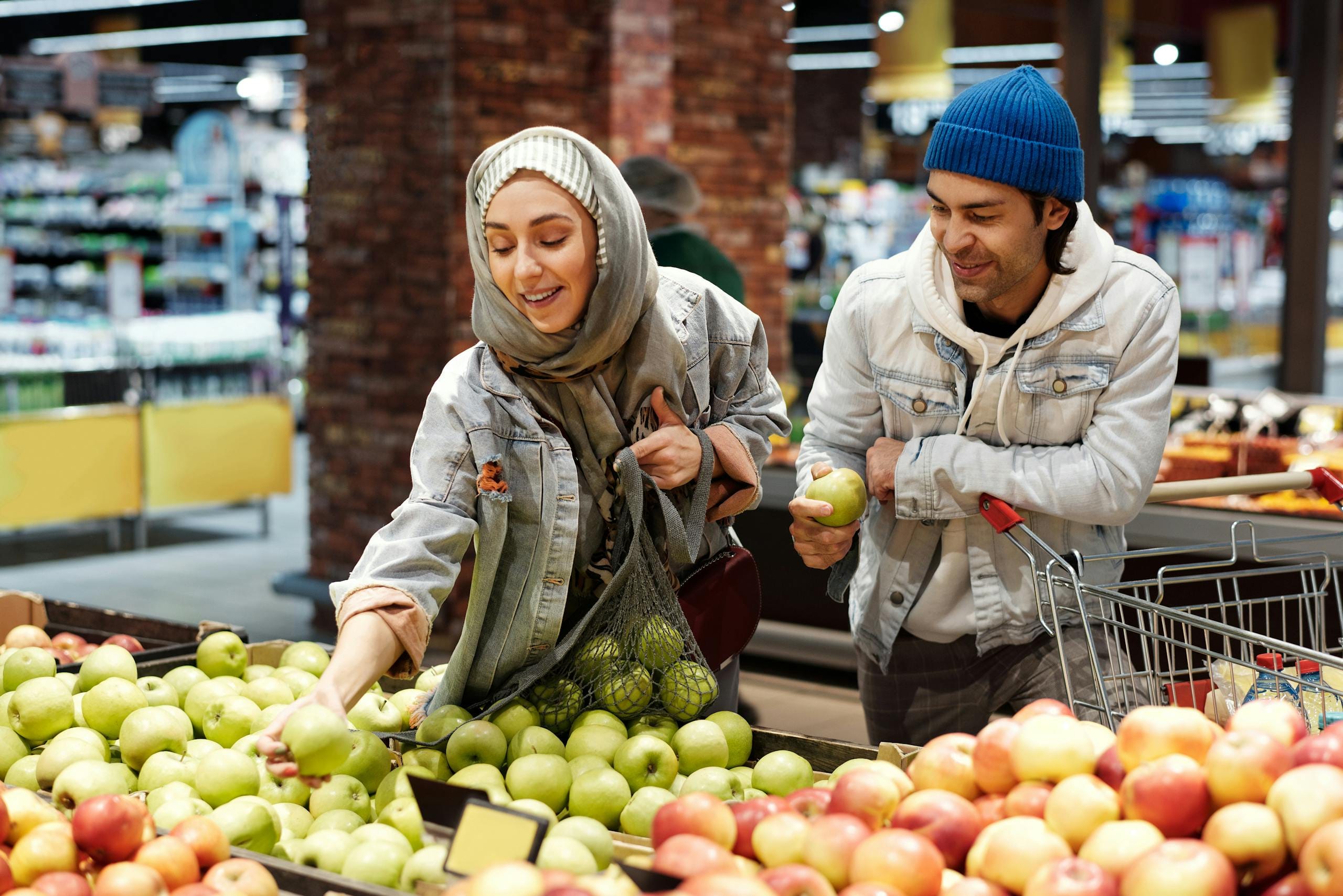 Muslim couple selects fresh apples at a supermarket, enjoying a shopping experience.