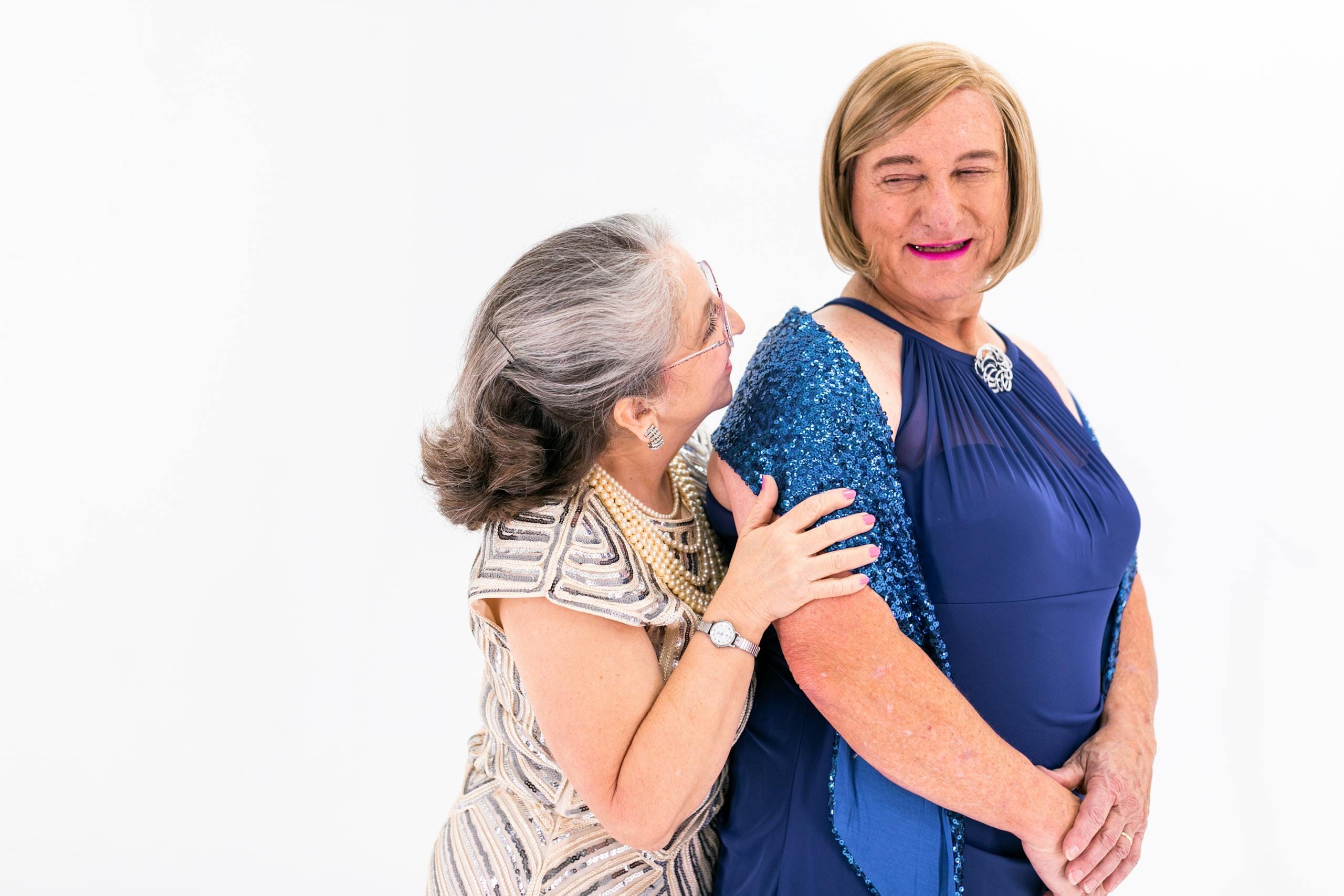 Two senior women joyfully embracing in elegant dresses, demonstrating love and togetherness.