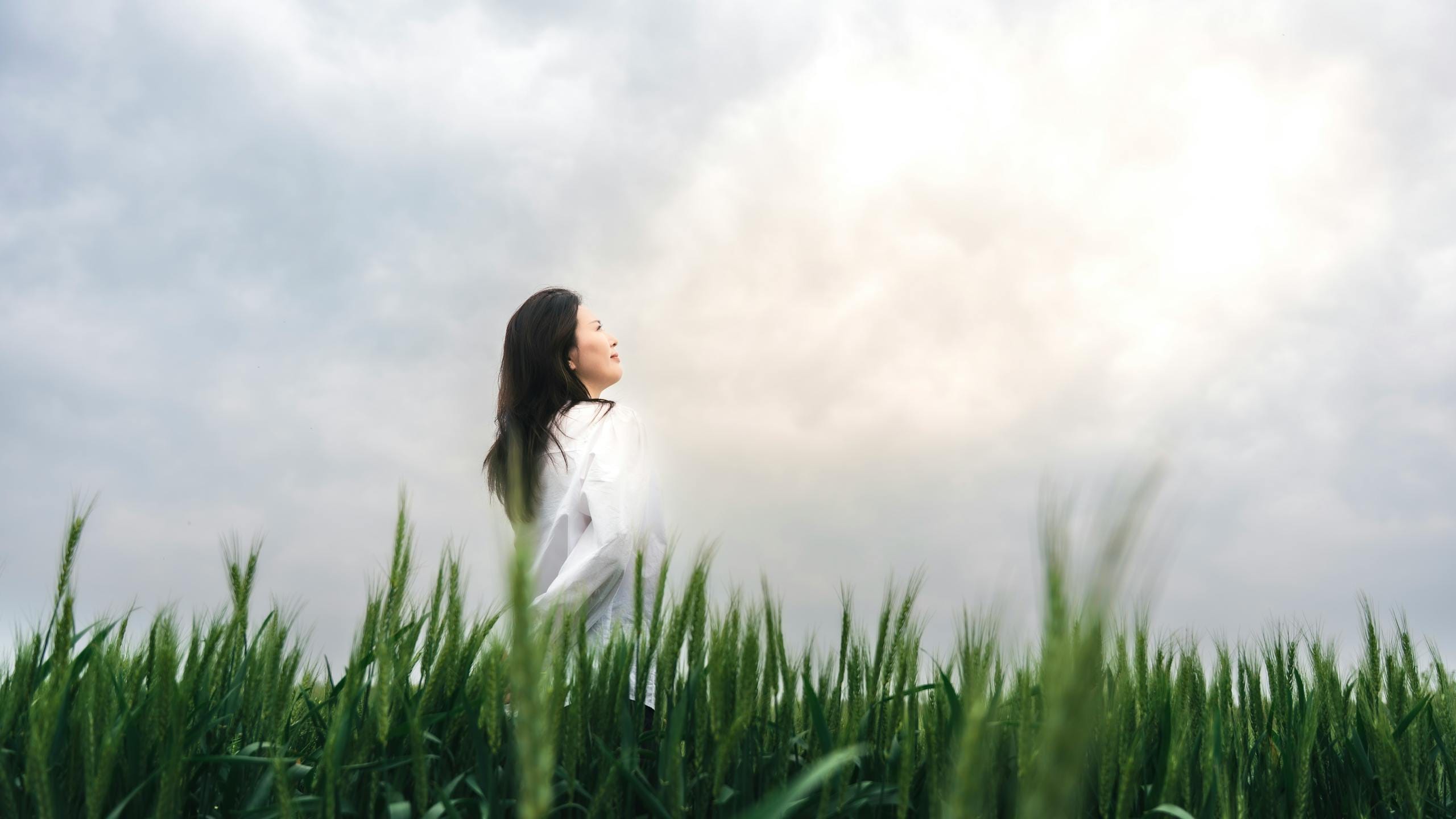 A serene scene of a woman enjoying nature in a lush green wheat field under a cloudy sky.