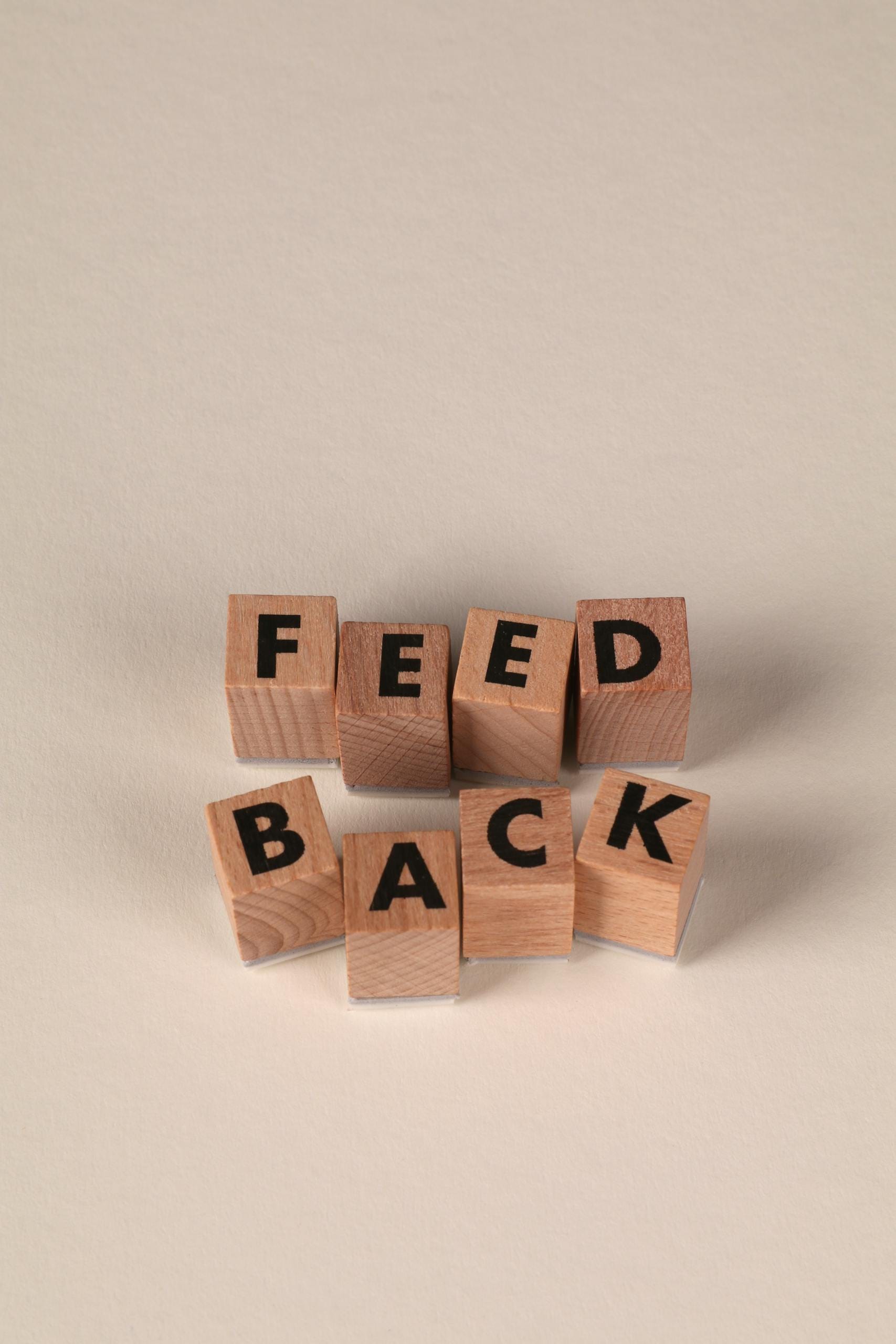 Wooden blocks forming the word 'Feedback' against a neutral beige background, conveying communication or review concept.