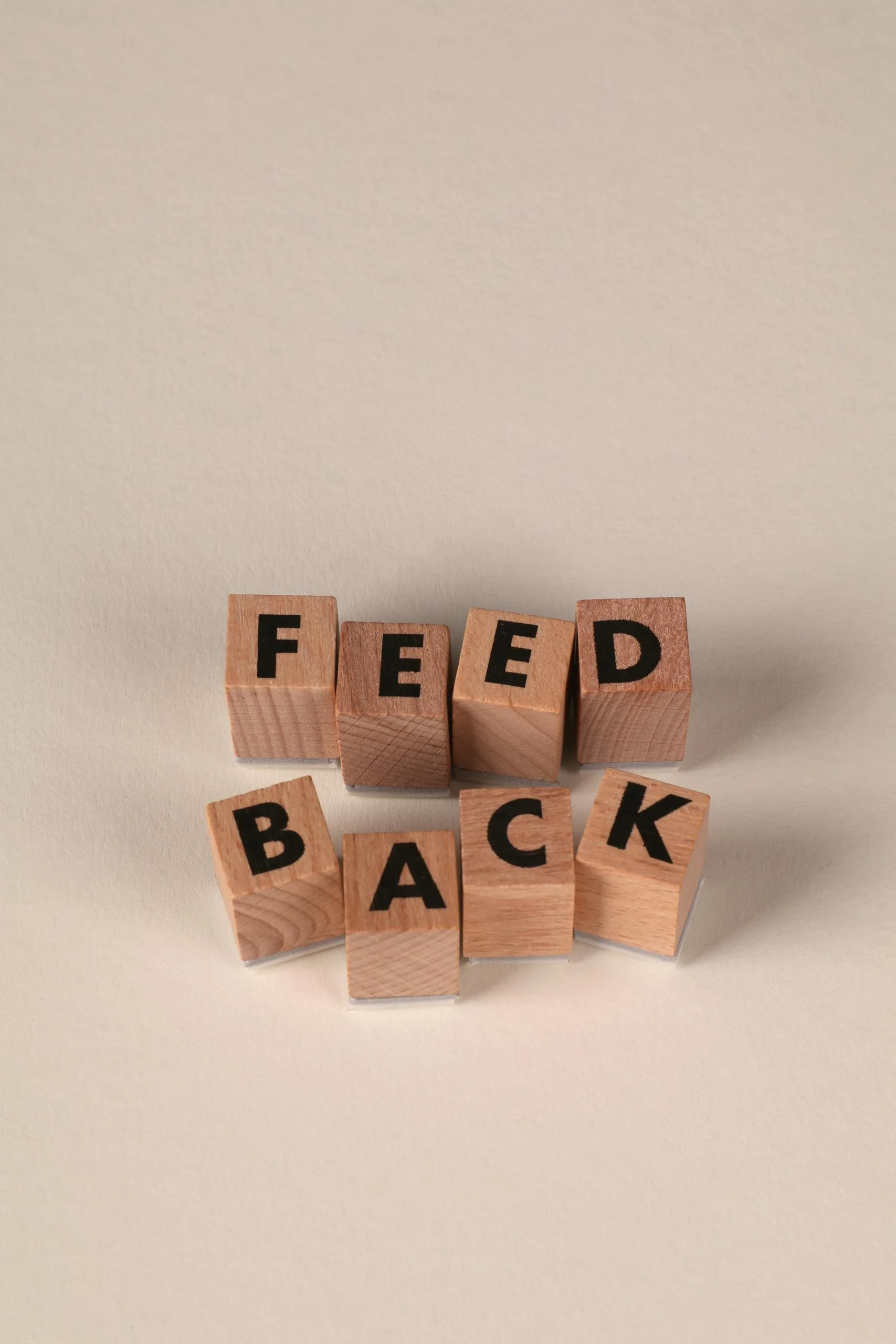 Wooden blocks forming the word 'Feedback' against a neutral beige background, conveying communication or review concept.
